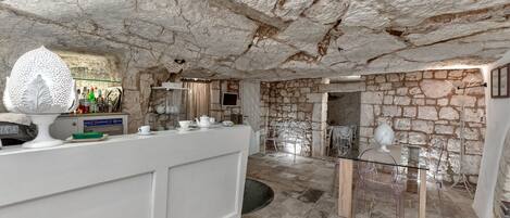 Una cocina con paredes de piedra, una encimera blanca, una mesa de vidrio y sillas transparentes.
