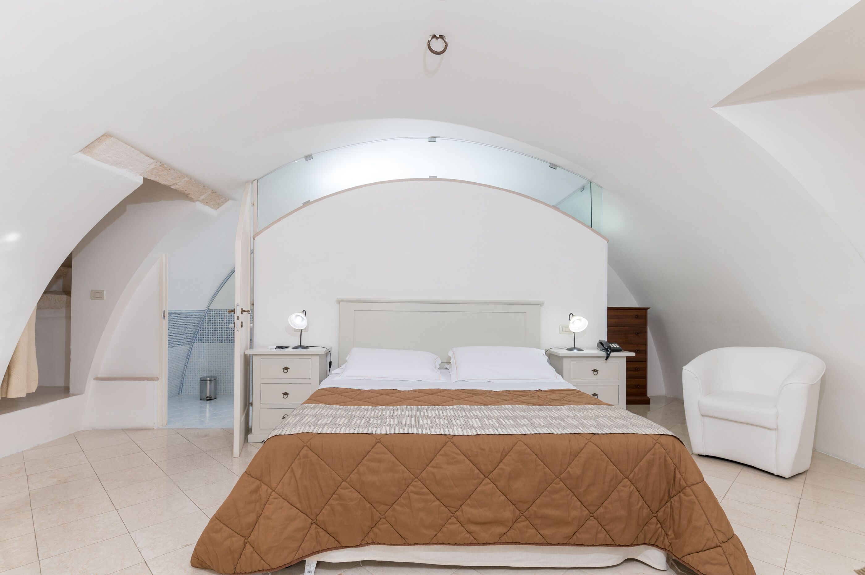 A bedroom with a bed, bedside tables, a chair, and a curved ceiling.