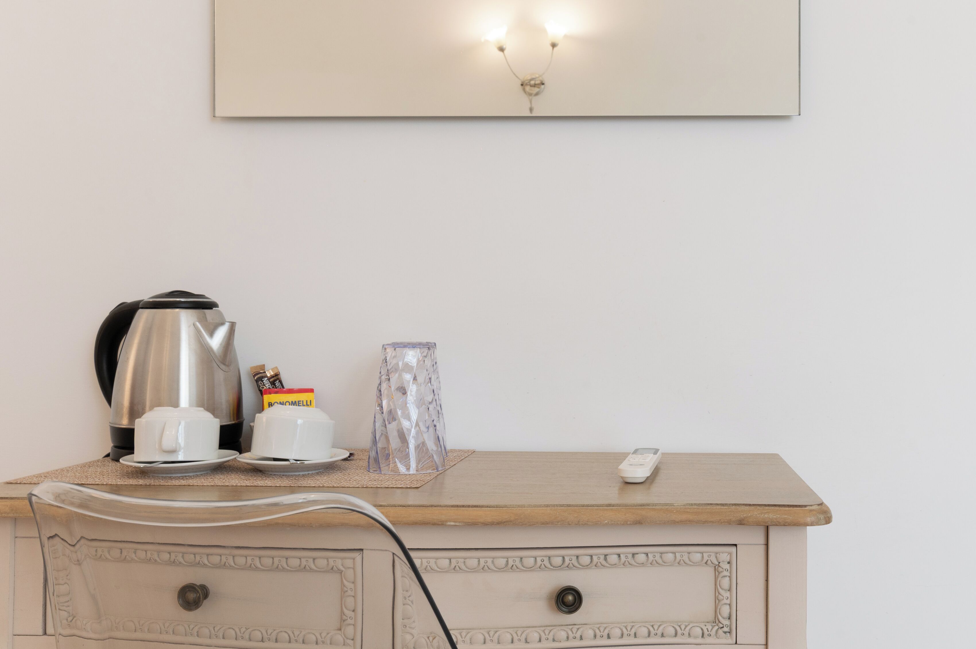 A kitchenette with a coffee maker, cups, a glass container, and a remote control on a wooden countertop.