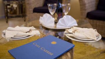 A dining table with a blue folder labeled "Casa Carrisi," two wine glasses, and white napkins on plates.