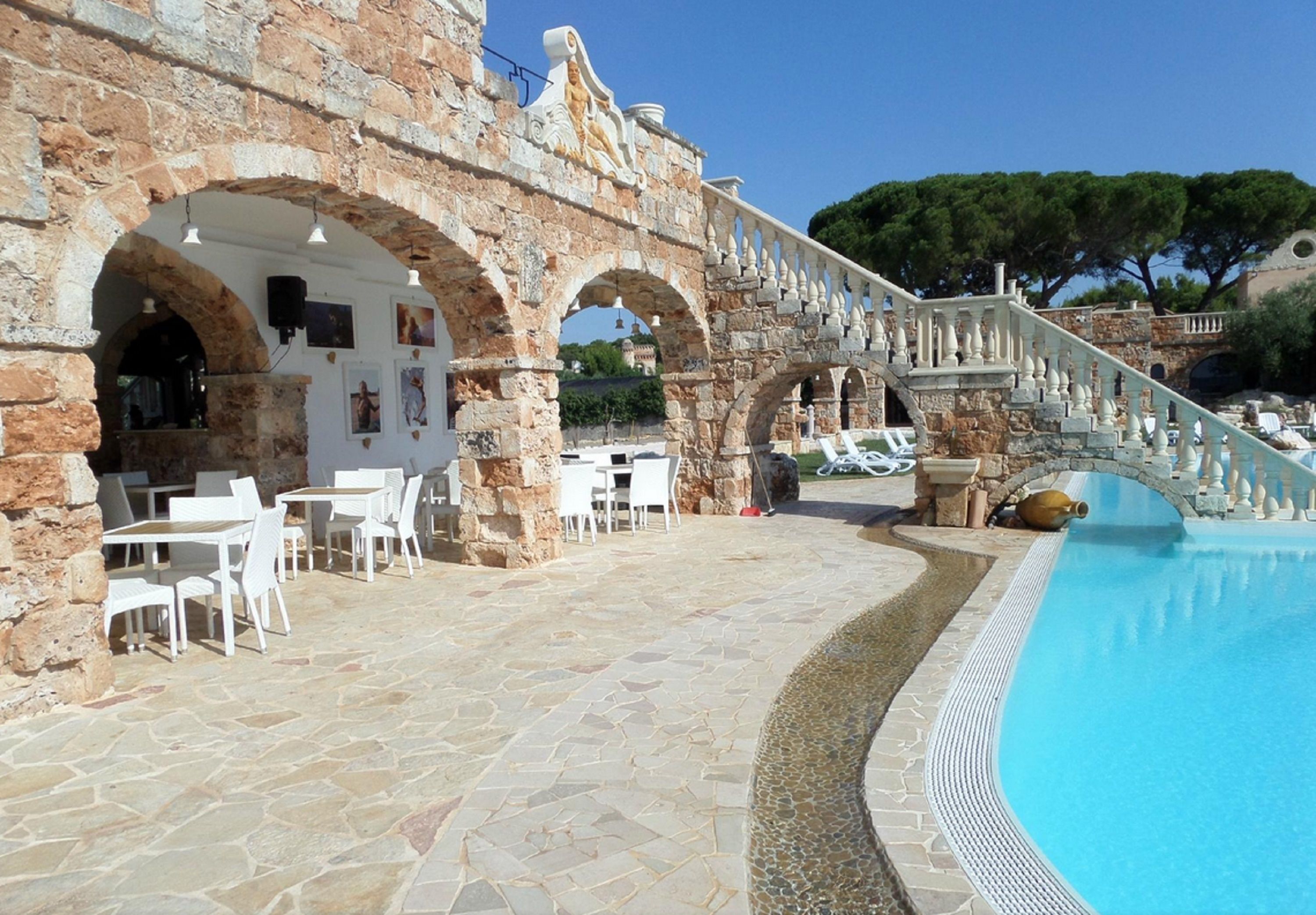 Un bâtiment en pierre doté d’arcades, d’une piscine et d’un espace extérieur aménagé pour s’asseoir.
