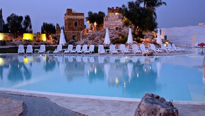 A pool with lounge chairs and umbrellas, a stone building with lights, and a rocky landscape. - Tenute Al Bano (Cellino San Marco)