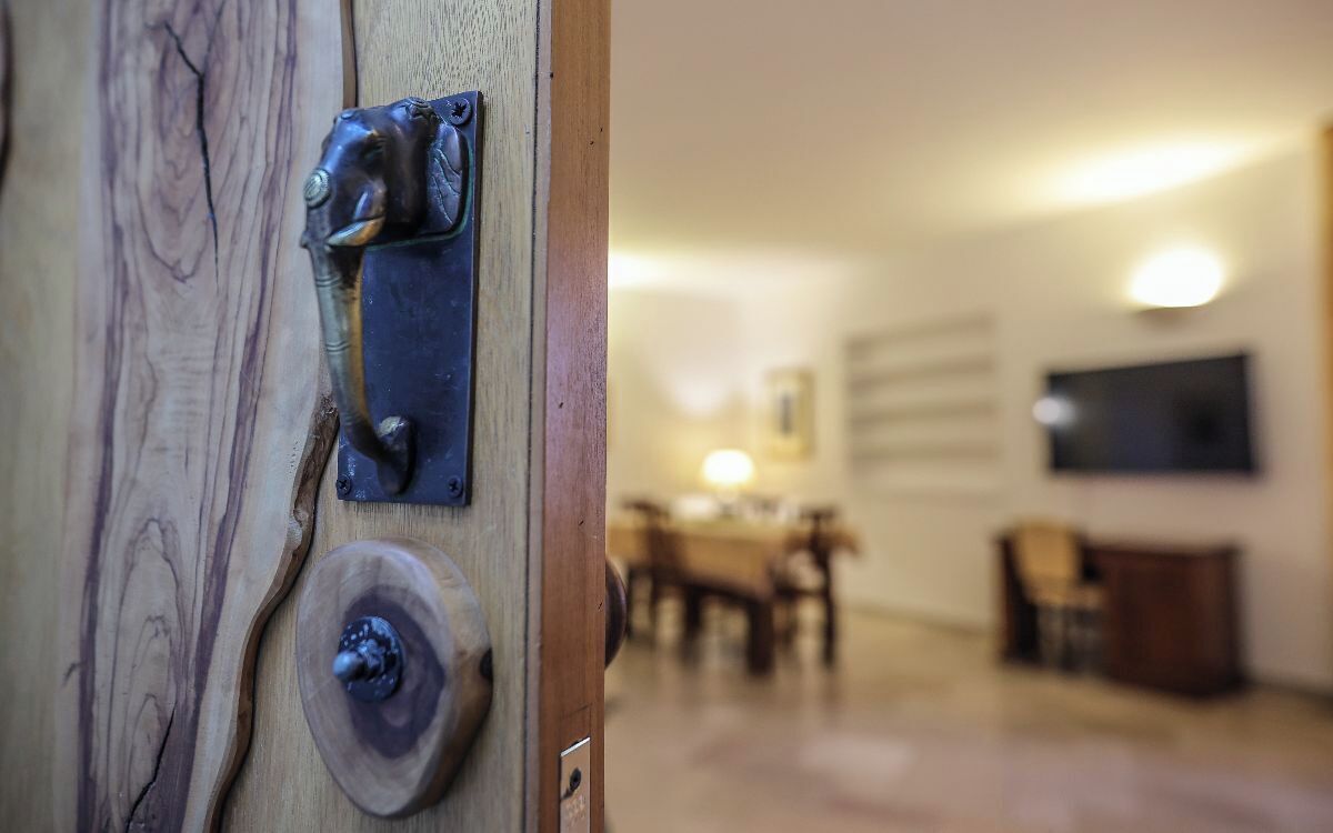 A wooden door with a metal handle and lock, leading into a room with a dining table and chairs.