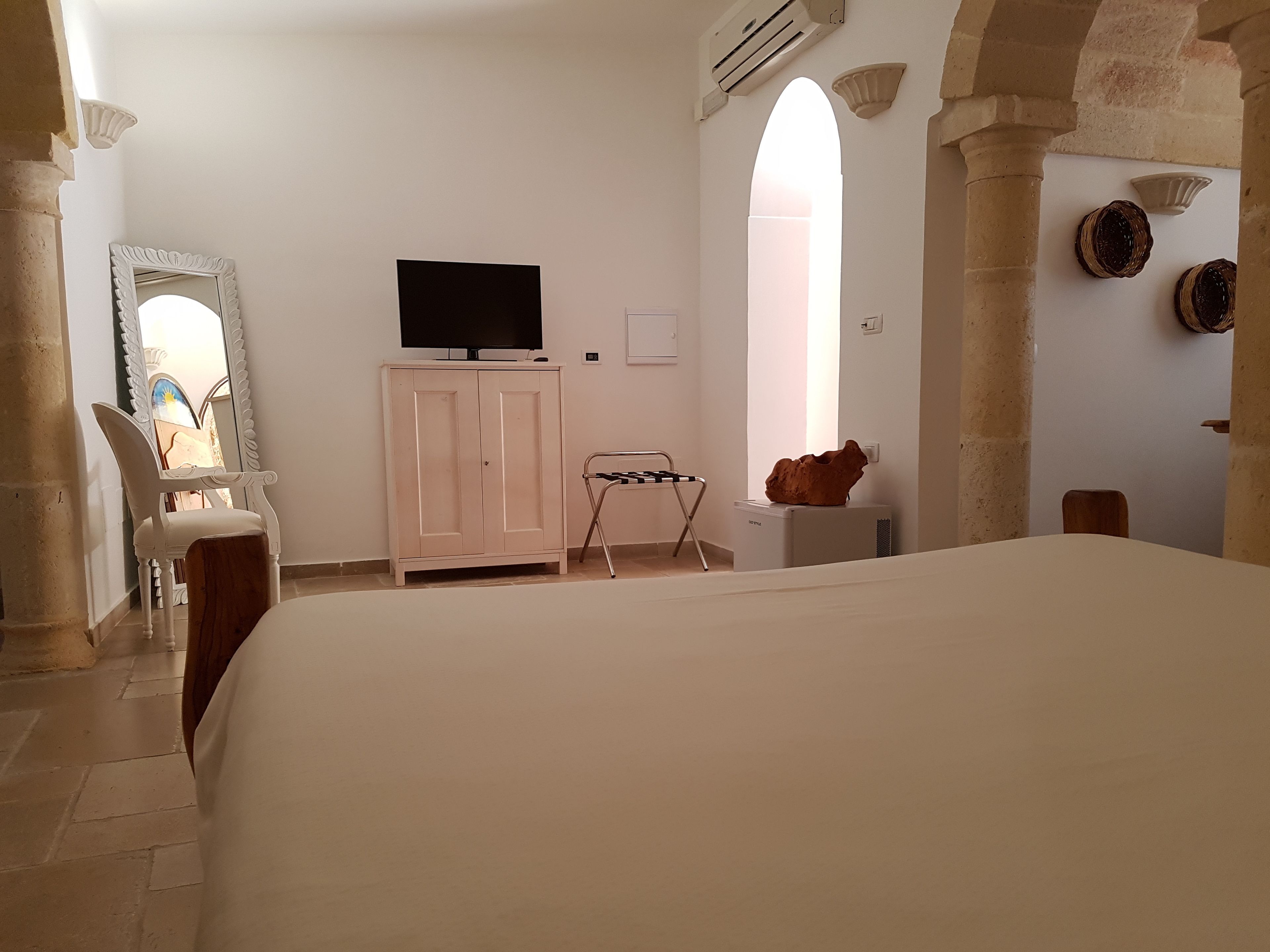 A bedroom with a bed, a TV on a cabinet, a chair, a small table, and a decorative item on the wall.