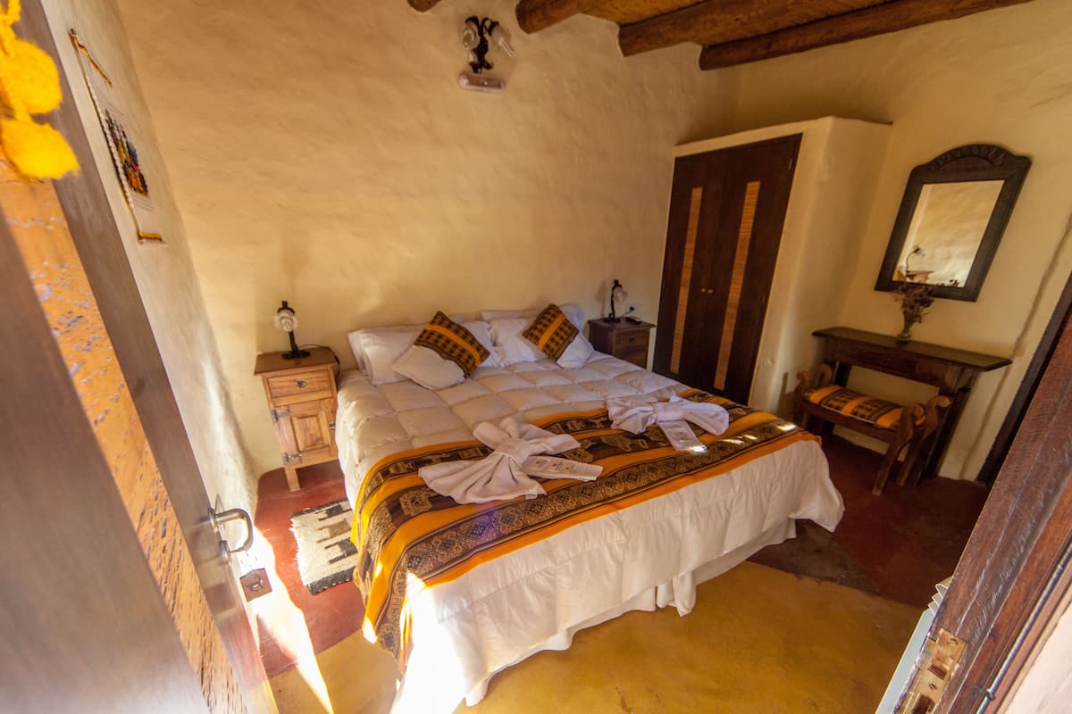 A bedroom with a large bed, a wooden nightstand, a bedside table, a mirror, and a wooden bench.