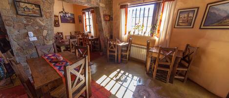 Un coin repas rustique avec des murs en pierre, des meubles en bois et une grande fenêtre agrémentée de rideaux.