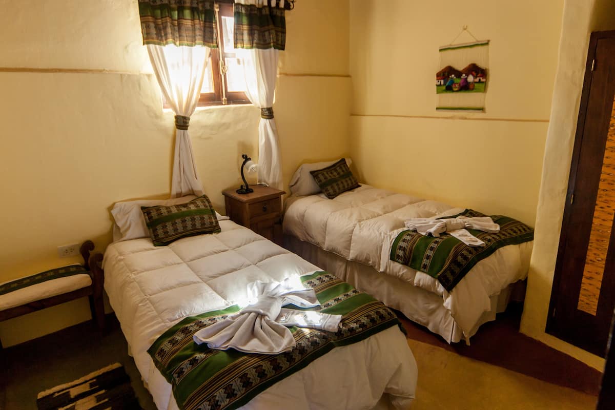A room with two beds, a bench, a nightstand, and a wall-mounted picture.