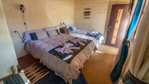 Una habitación con dos camas, suelo de madera, una puerta y un aplique en la pared.