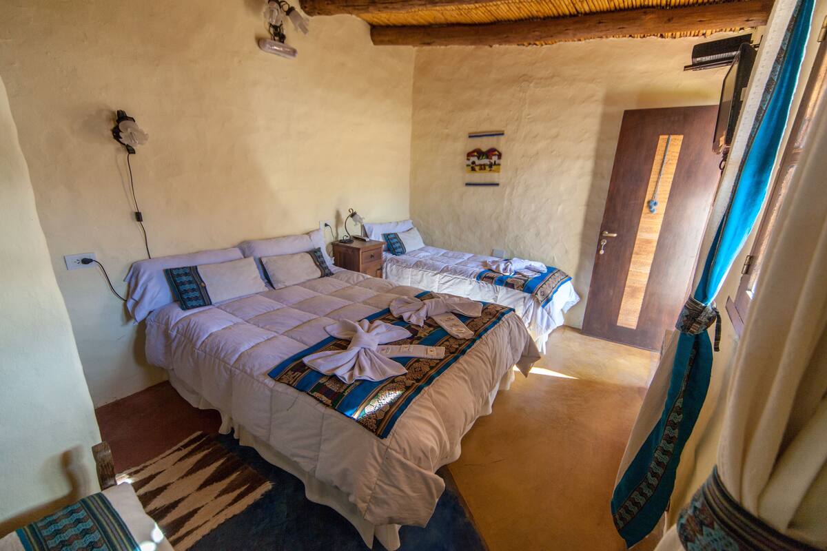 A room with two beds, a wooden floor, a door, and a wall-mounted light fixture.