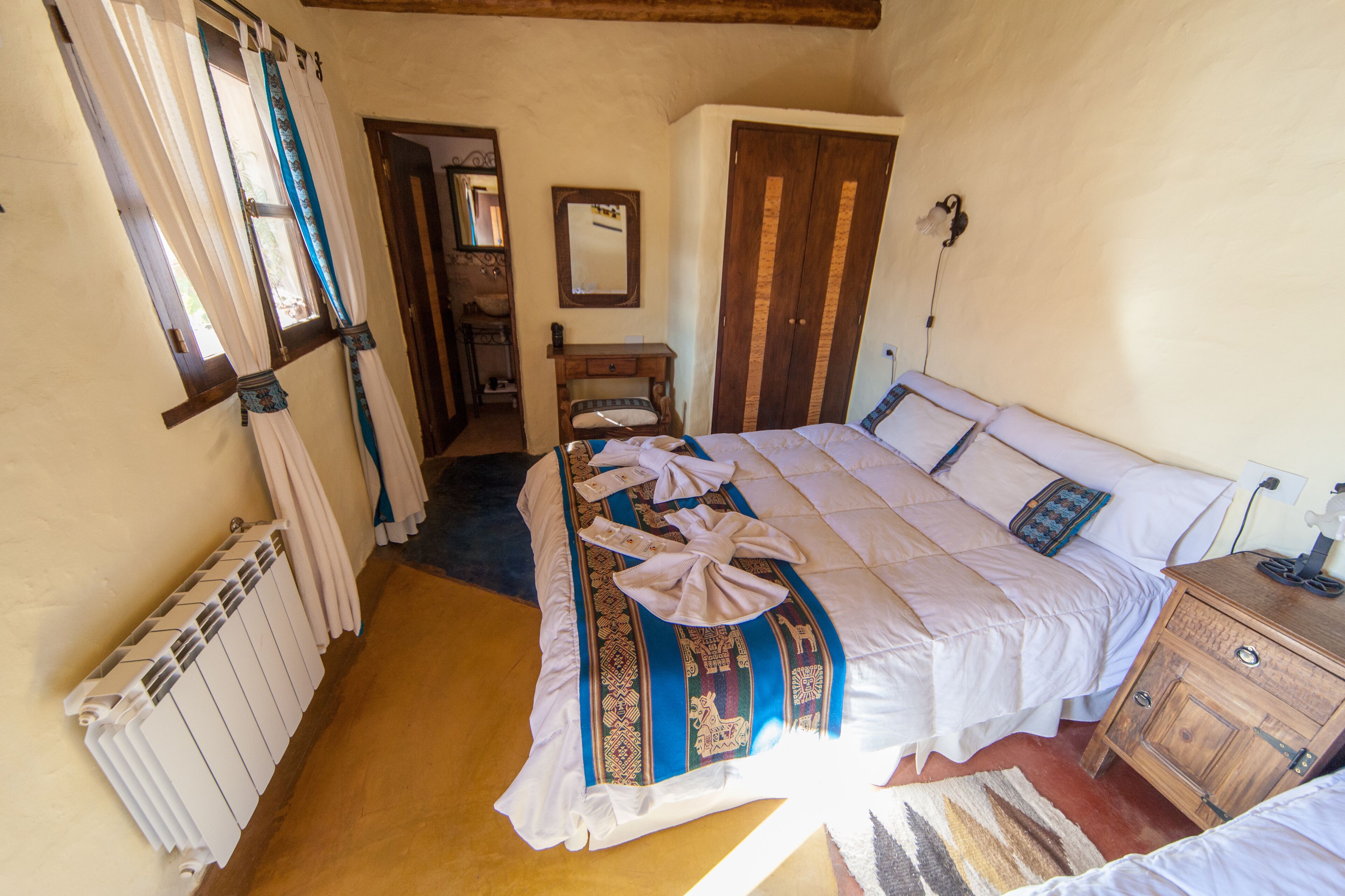 A bedroom with a bed, a wooden nightstand, a dresser, a mirror, and a radiator.