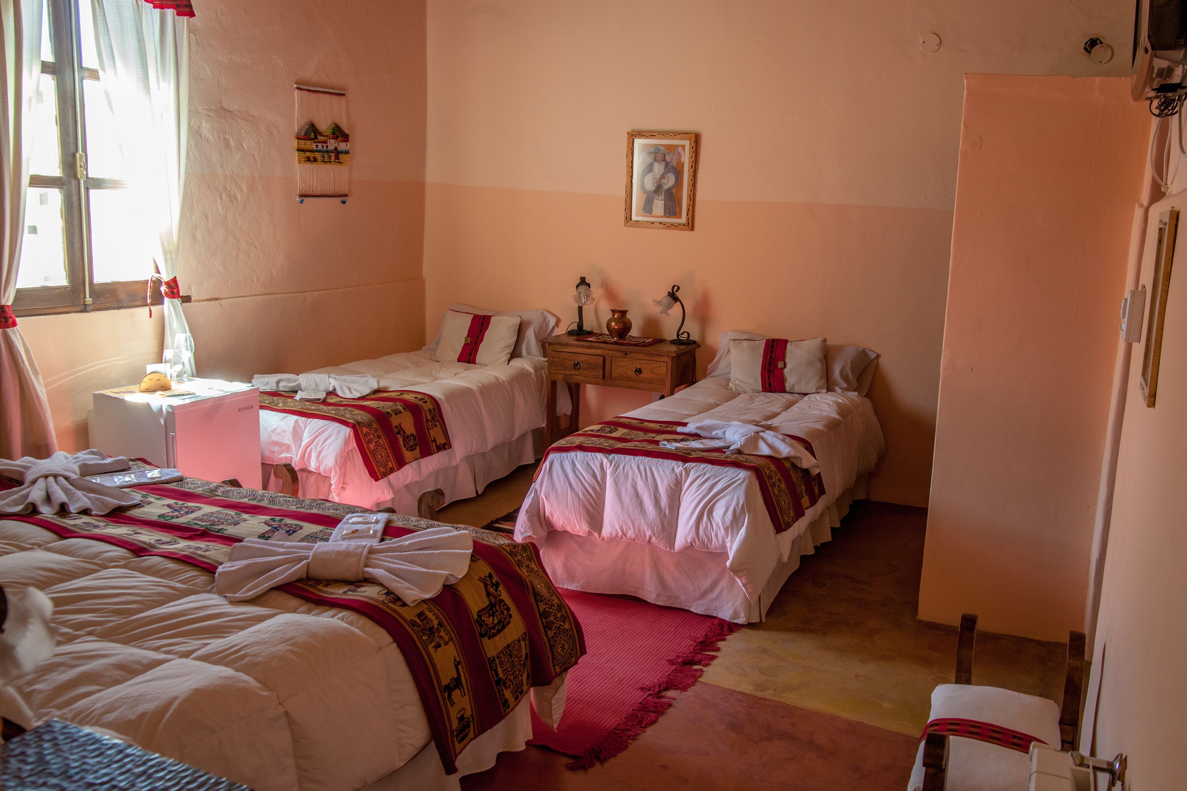 Habitación de hotel con dos camas, una mesita de noche de madera, una pequeña mesa y una ventana con cortinas.