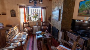 Una sala de estar acogedora con pared de piedra, chimenea, televisor y zona de estar confortable con un banco y sillas.