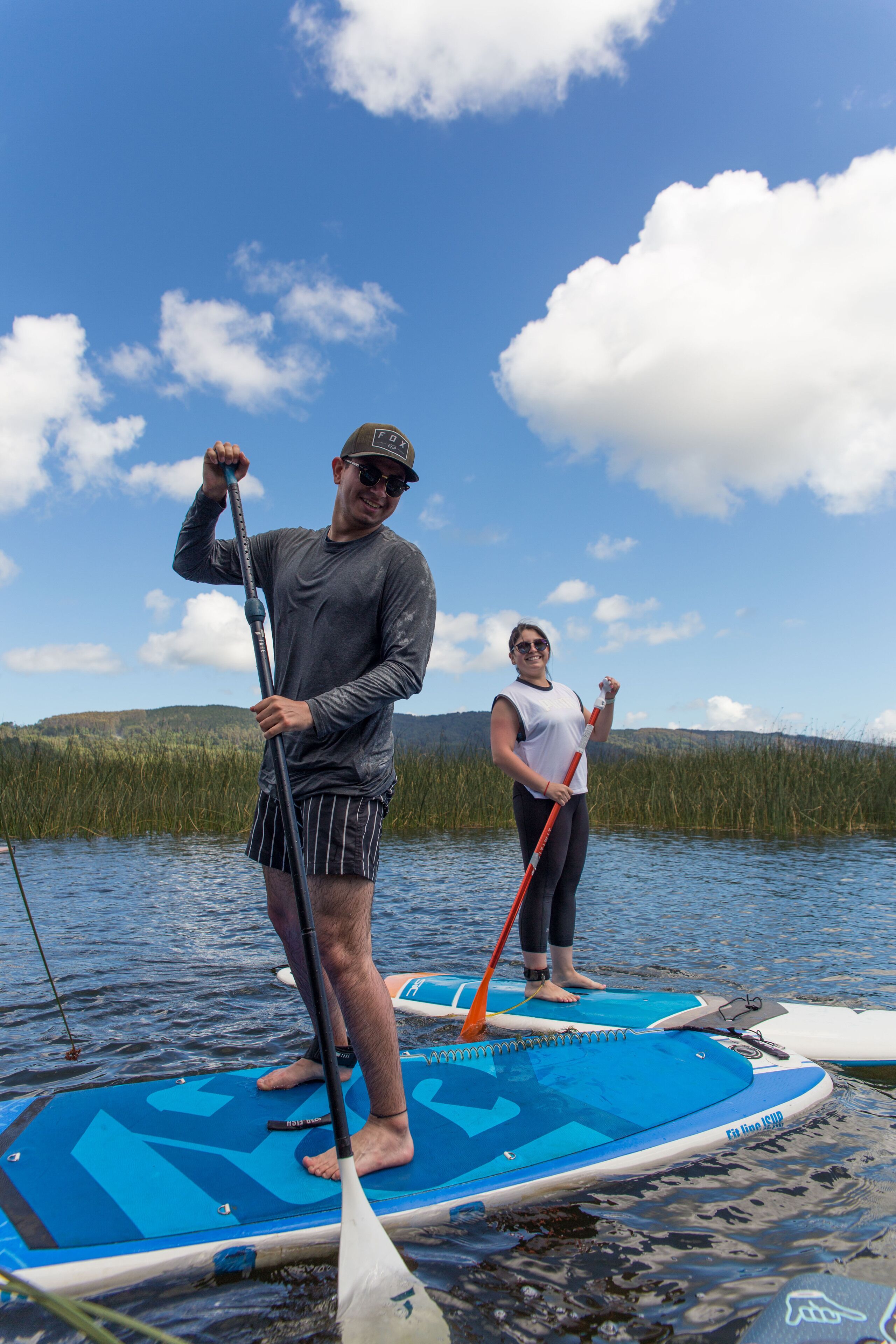 Two people on paddleboards in a calm lake with a forested background.