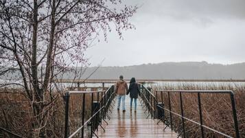 A wooden boardwalk with metal railings, leading to a body of water with a distant shoreline.