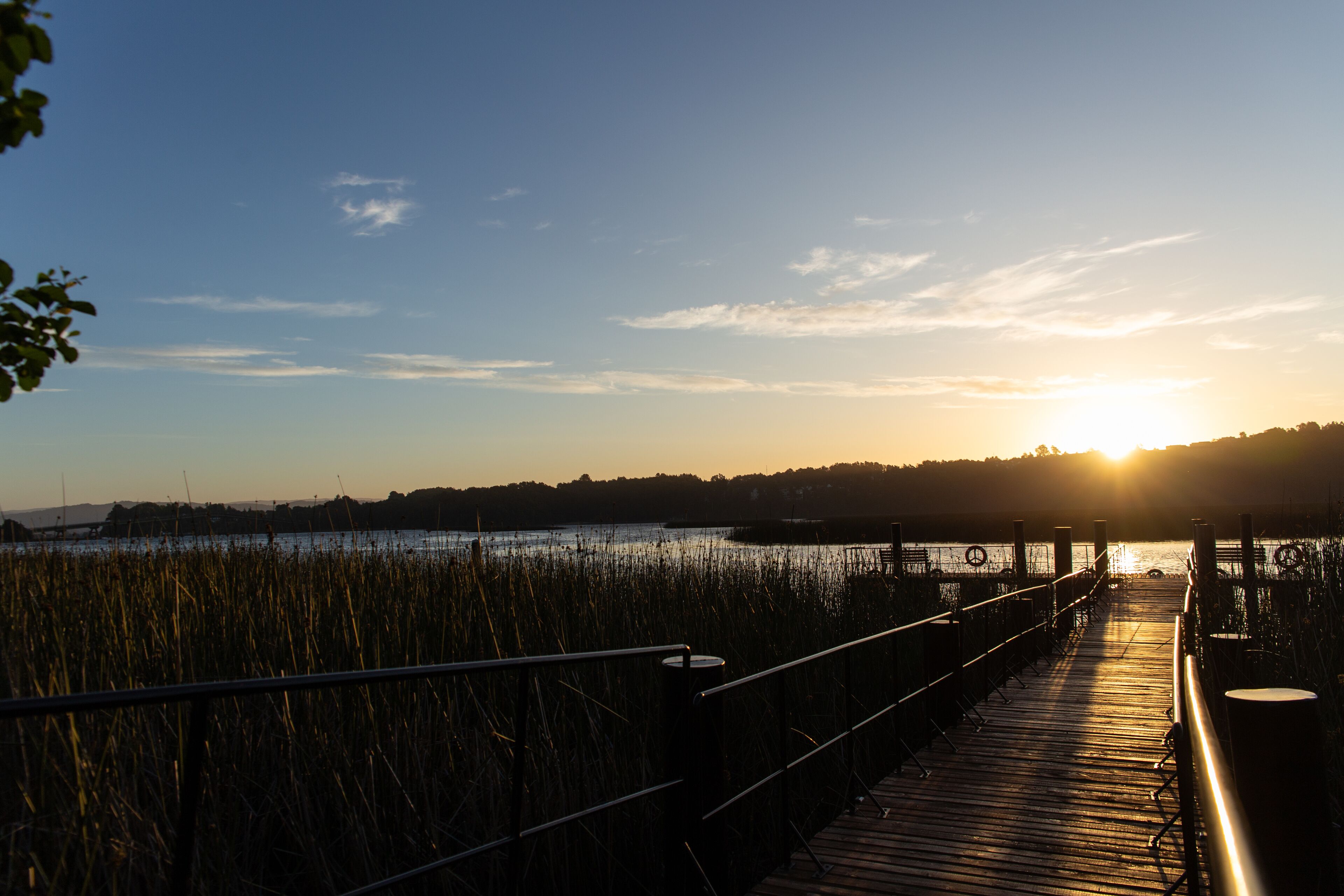 Una passerella in legno che conduce a uno specchio d'acqua sullo sfondo di un tramonto.