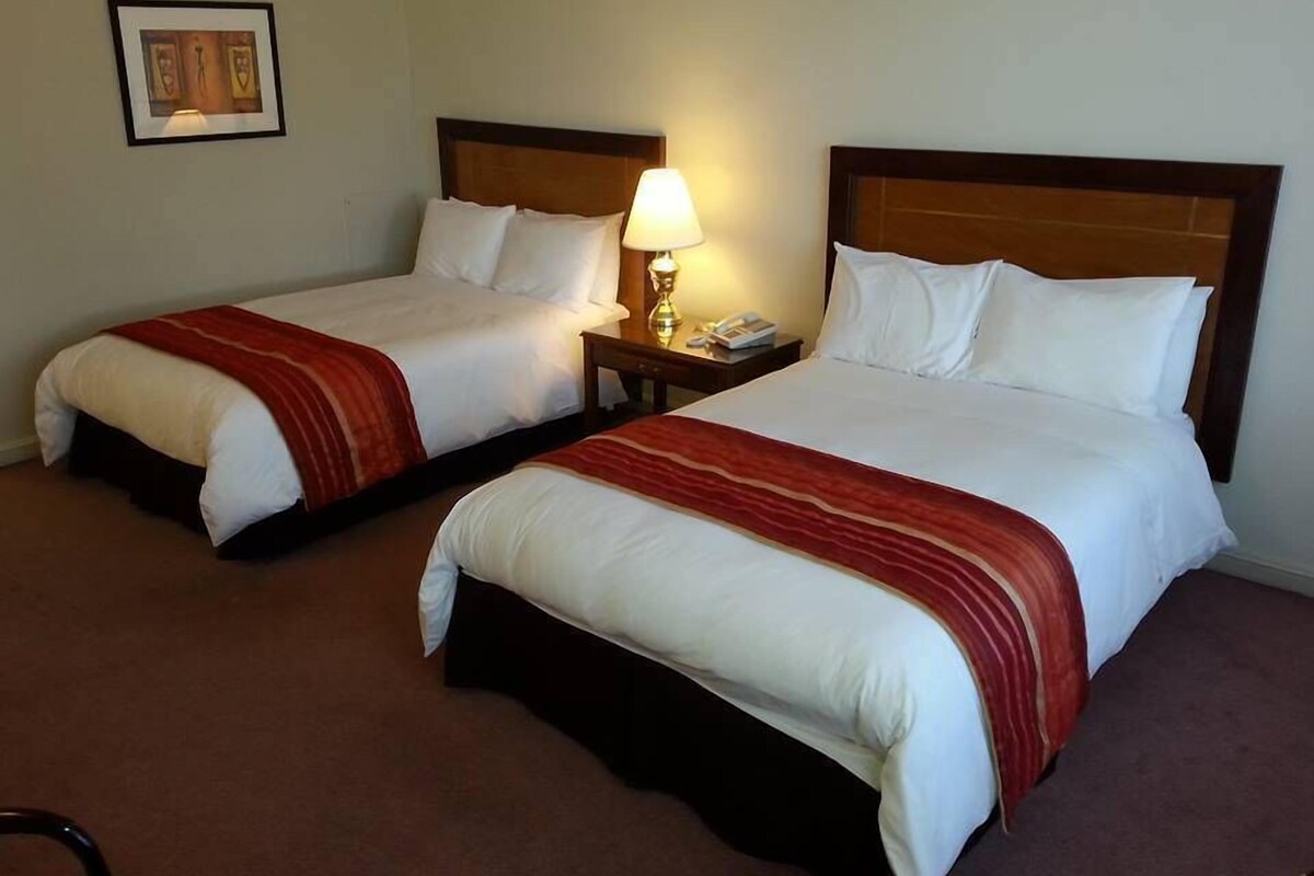 Two double beds with white linens and red striped bedspreads in a hotel room.