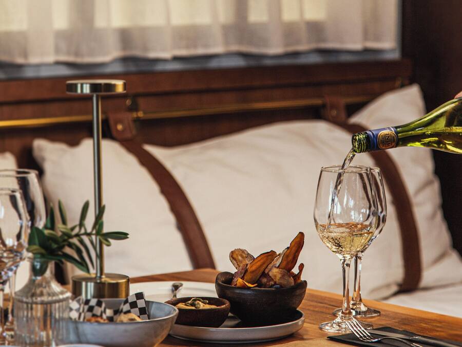 A dining table with a bottle of wine being poured into a glass, a bowl of food, and various dishes and utensils.