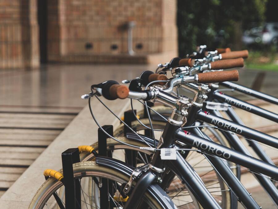 A row of bicycles parked in a covered area with a brick building in the background.
