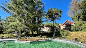 Una piscina cristalina rodeada de sillas de descanso y un área boscosa, con un edificio al fondo.