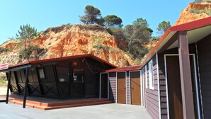 A building with a wooden exterior and a red roof, situated in a natural landscape with red rock formations and sparse vegetation. - Aldeia da Falésia (Albufeira)