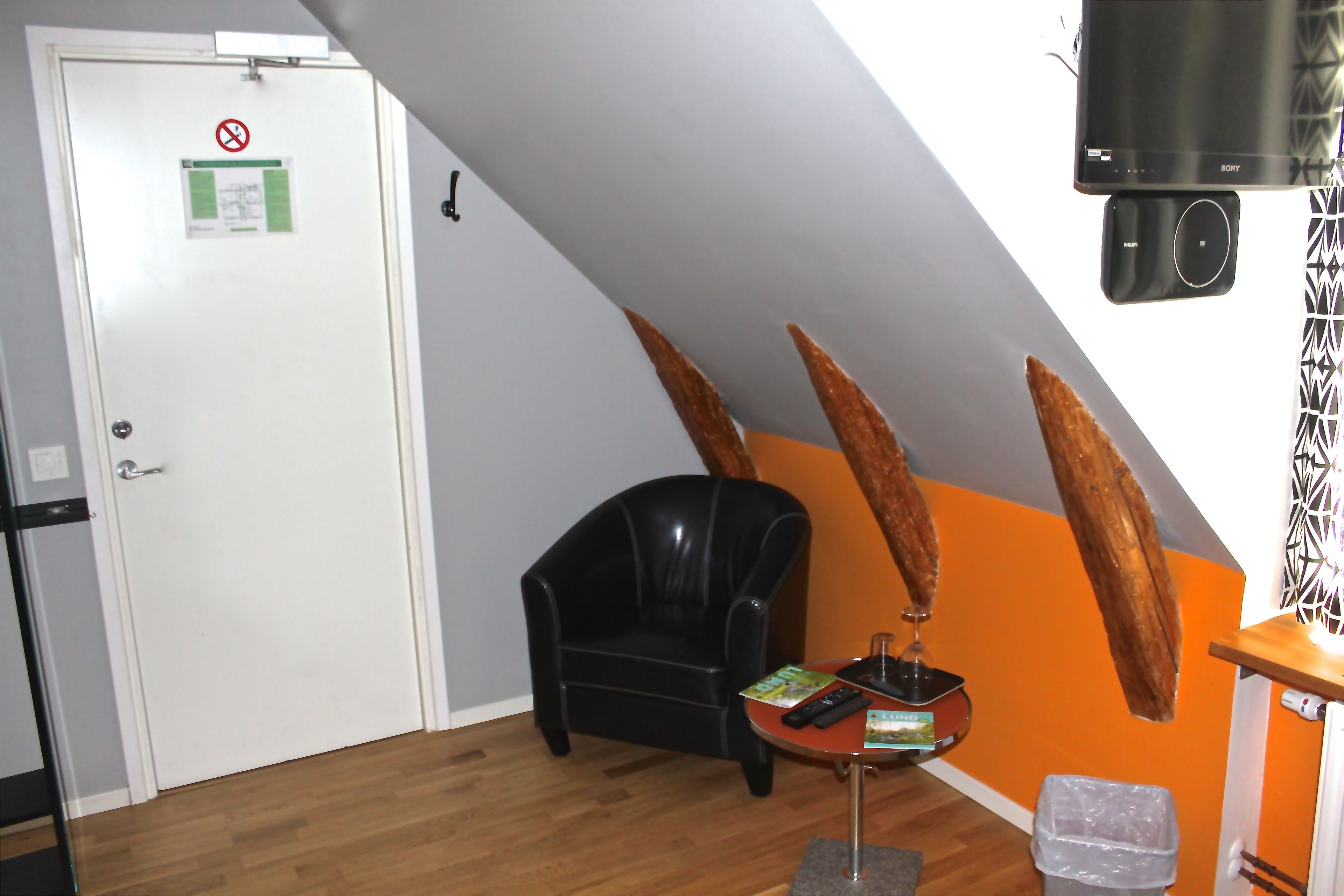 Una habitación con un sillón de cuero negro, una mesita con un control remoto, un televisor y una puerta con el cartel de prohibido fumar.