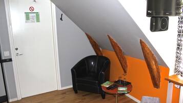 Una habitación con un sillón de cuero negro, una mesita con un control remoto, un televisor y una puerta con el cartel de prohibido fumar.