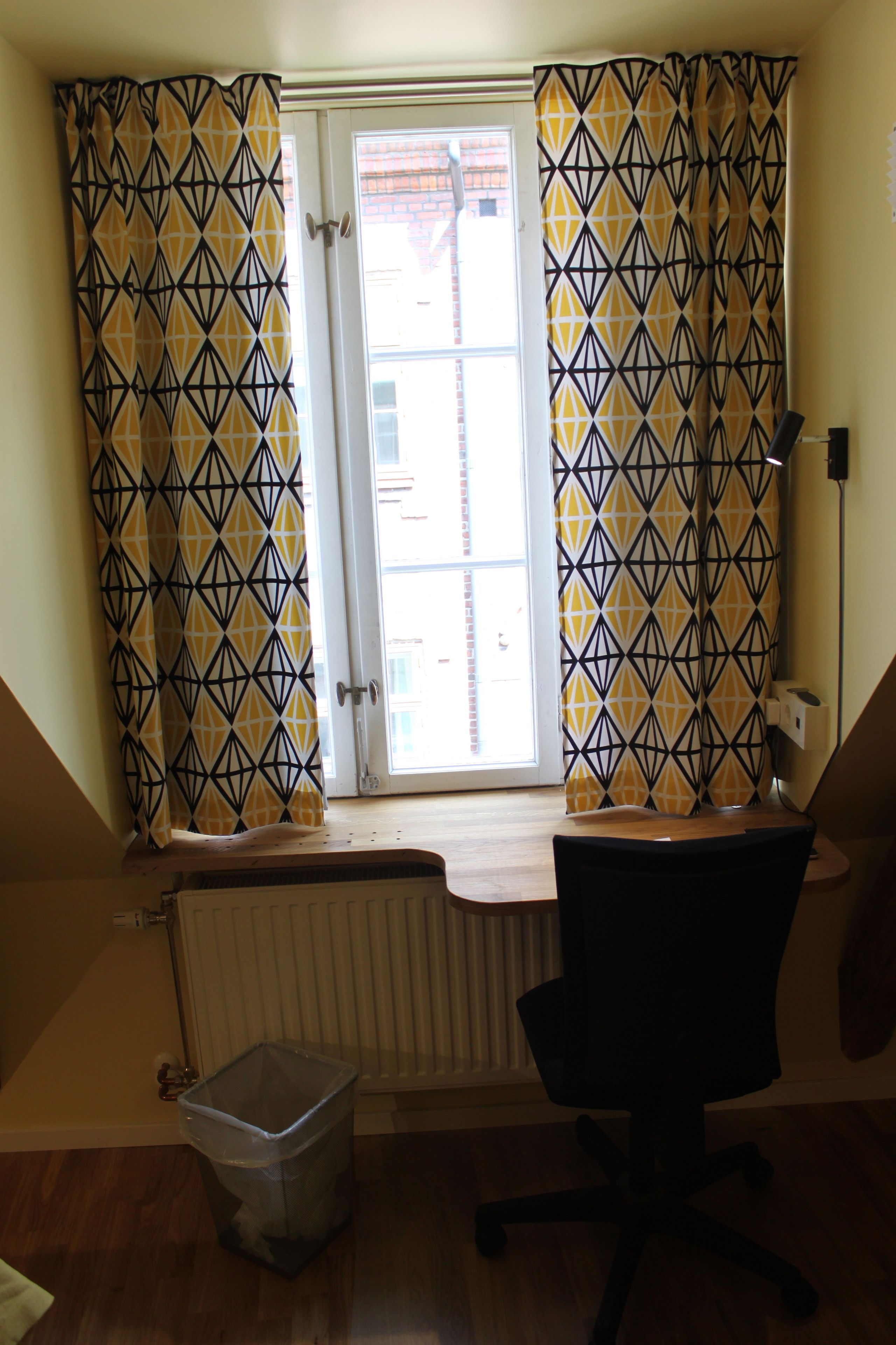 A room with a window, radiator, trash bin, and office chair.