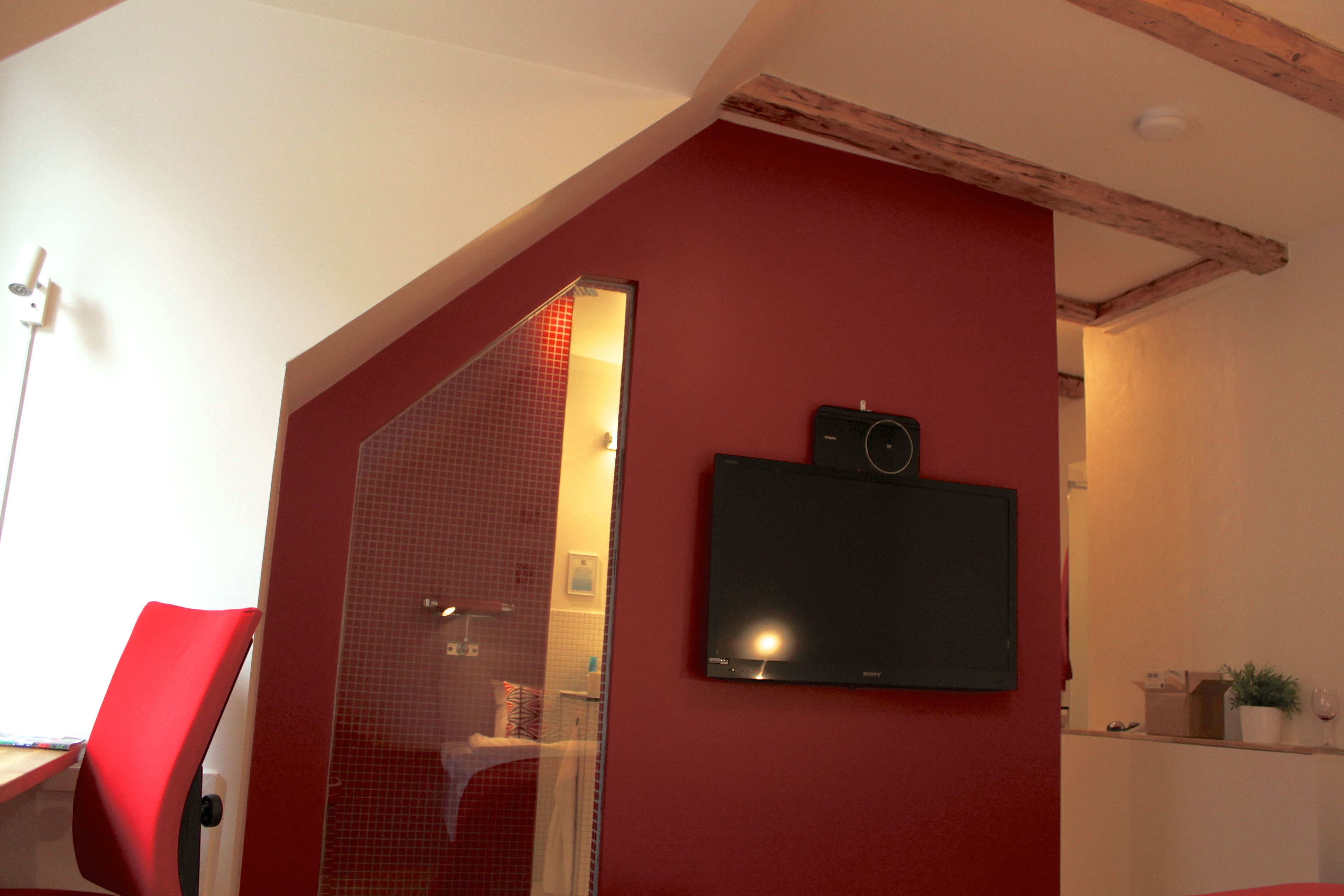 A room with a red wall, a mounted television, and a red chair.