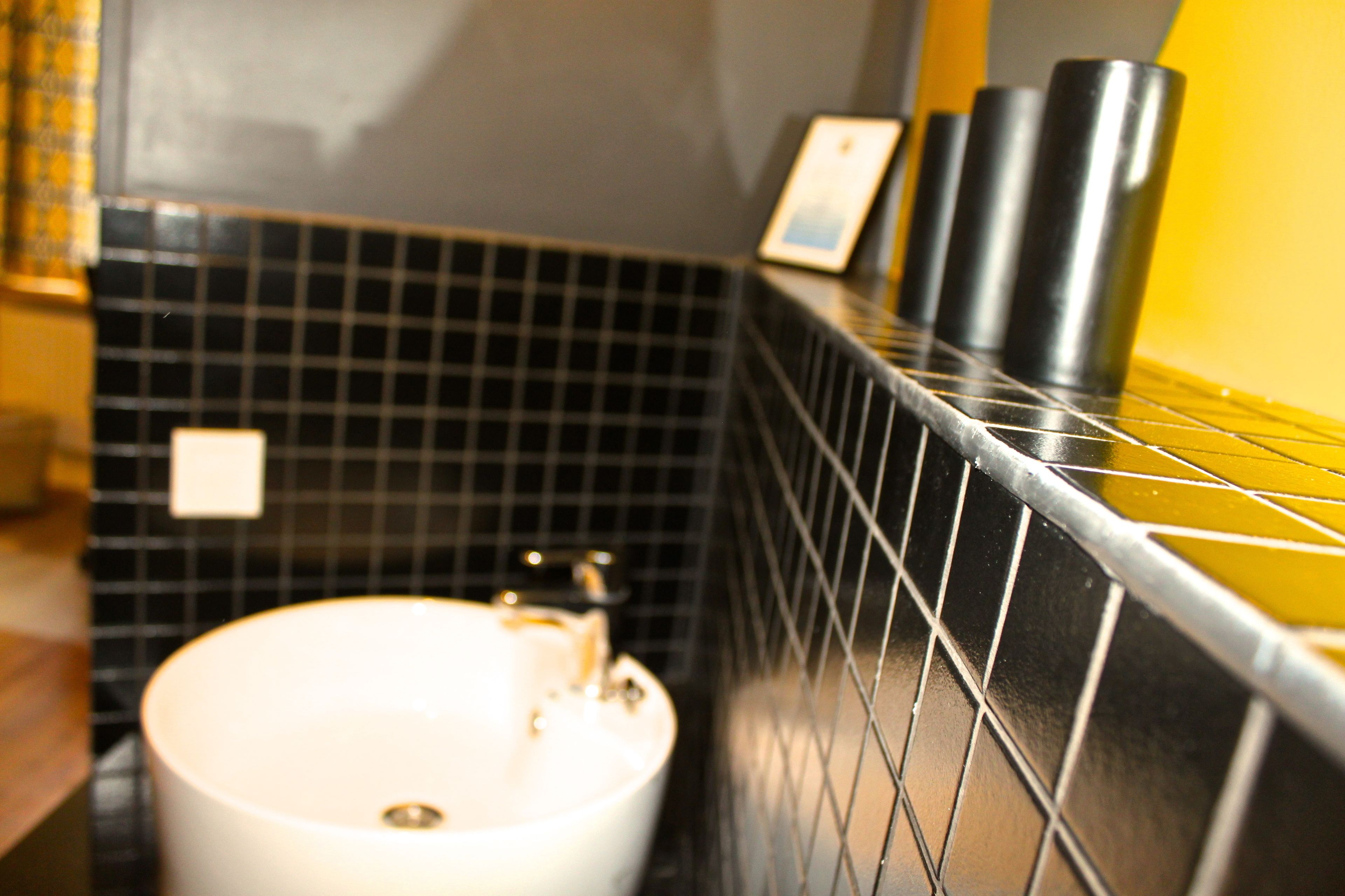 Un baño con lavamanos blanco, paredes cubiertas de azulejos negros y una pared de acento amarilla.