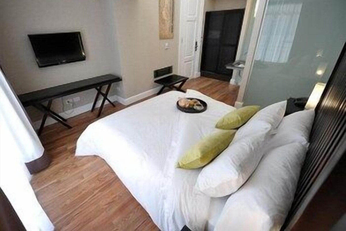 A hotel room with a bed, a desk, a chair, a television, and a door leading to another room.