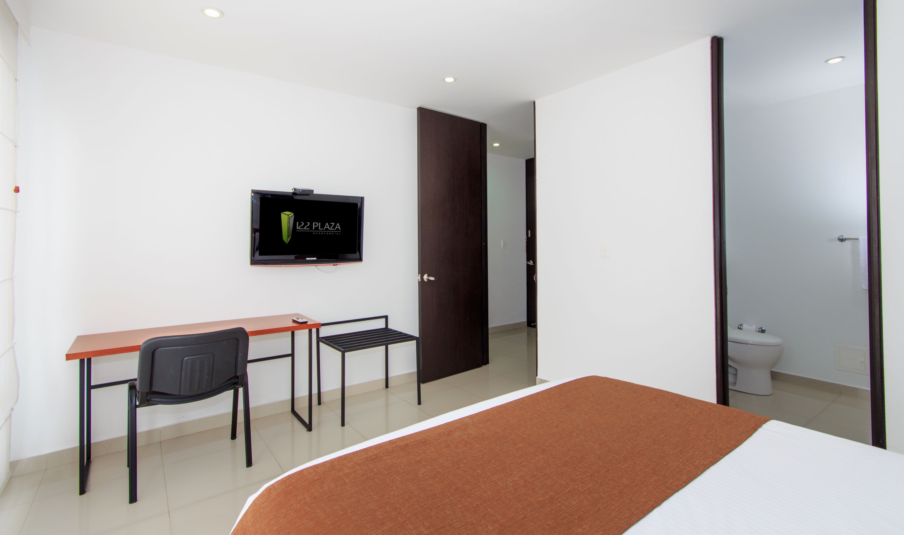 Un dormitorio con cama, escritorio, silla, televisor y baño.