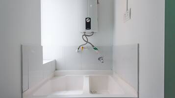 Un baño con una bañera blanca, un inodoro blanco y un lavamanos blanco. Cuenta con un calentador blanco instalado en la pared y un enchufe eléctrico blanco.