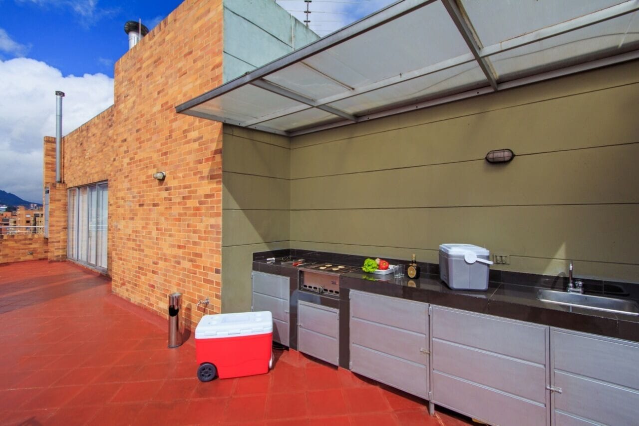 Un patio en la azotea con pared de ladrillo, una parrilla, un lavamanos y un enfriador.