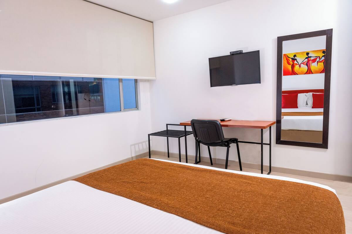Een hotelkamer met een bed, bureau, stoel, televisie en raam.