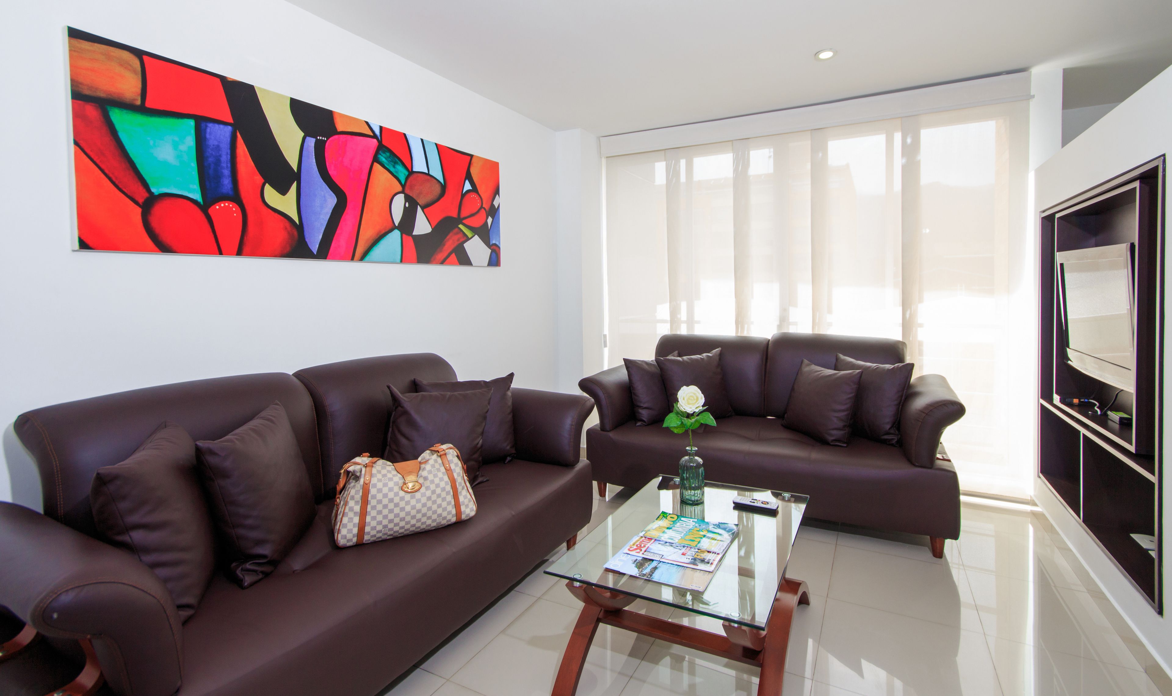 A modern living room with two brown leather sofas, a glass coffee table, and a large abstract painting on the wall.