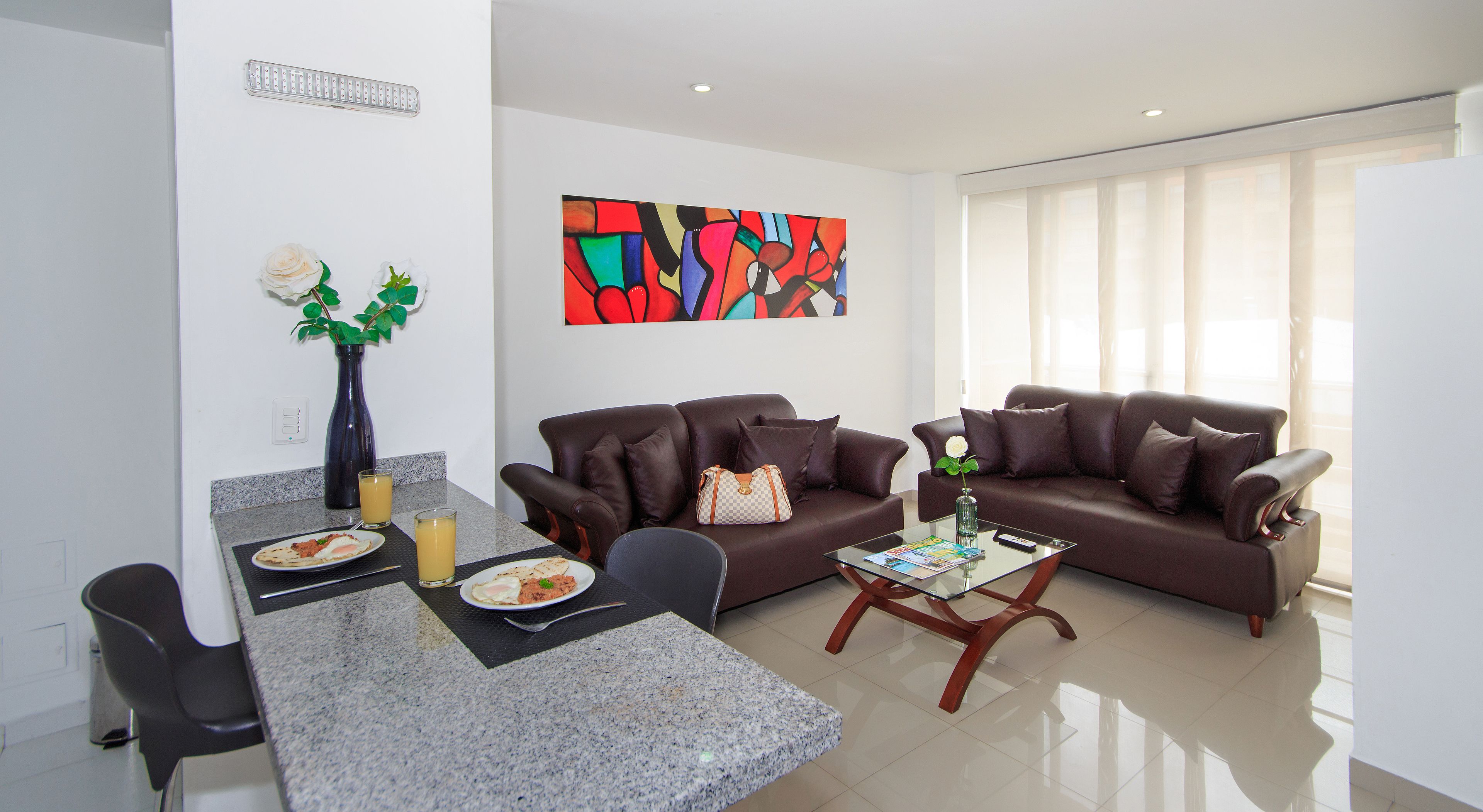 Una sala de estar moderna con un sofá de cuero marrón, una mesa de centro de vidrio y un comedor con una mesa de granito.