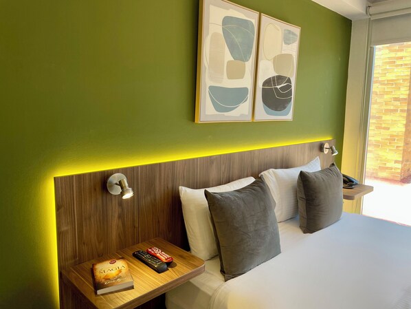 A hotel room with a wooden headboard, a bedside table with a remote control, a book, and a pillow.