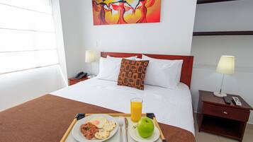 Habitación de hotel con cama, mesitas de noche, una bandeja de desayuno y un cuadro en la pared.