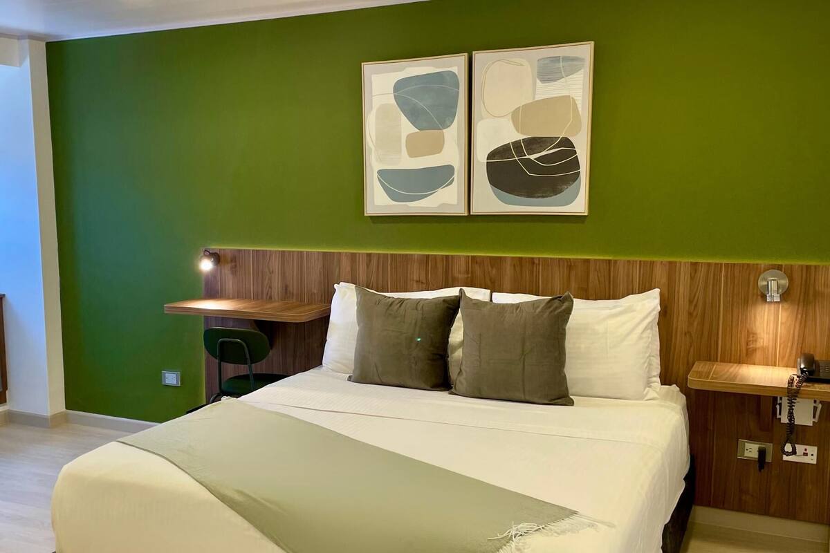 Een hotelkamer met een bed, een bureau en twee abstracte schilderijen aan de muur.