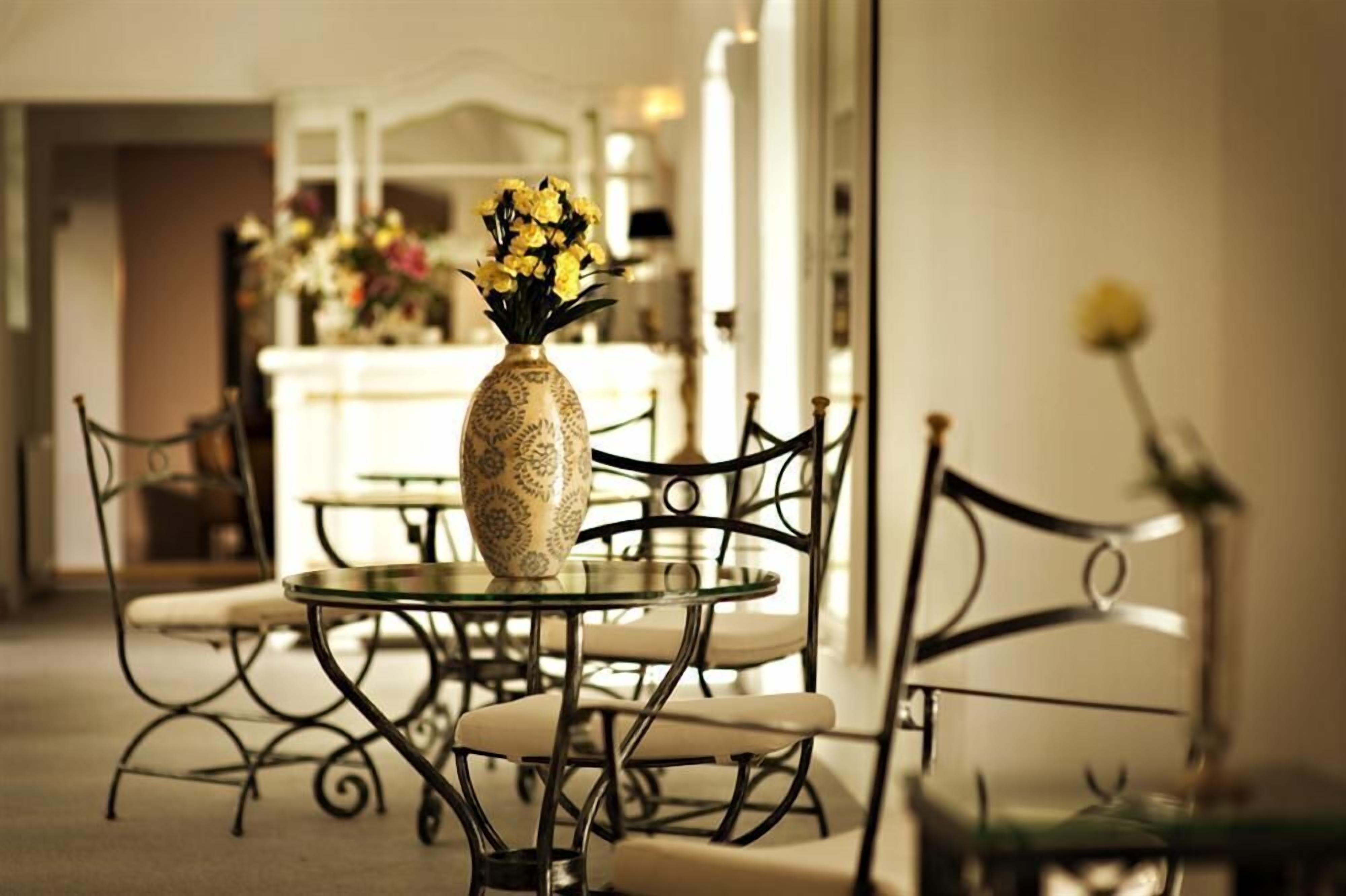 A dining area with a glass table and chairs, a vase with yellow flowers, and a mirror reflecting the room.