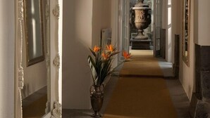 Un pasillo con espejos de marco blanco ornamentado, una urna central y suelo alfombrado.