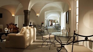 Un salón espacioso con un techo alto abovedado, un sofá cómodo, una mesa de centro de vidrio y una zona de comedor al fondo.