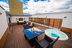 A rooftop deck with a glass-top table, black wicker chairs, a hot tub, and a view of buildings. - Hotel Golden Palermo (Medellín)