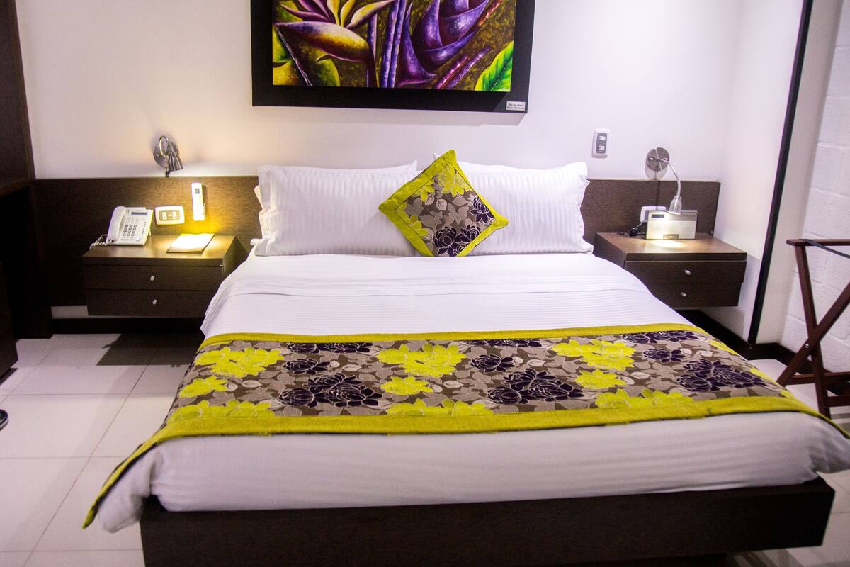 A hotel room with a bed, nightstands, a telephone, and a painting on the wall.