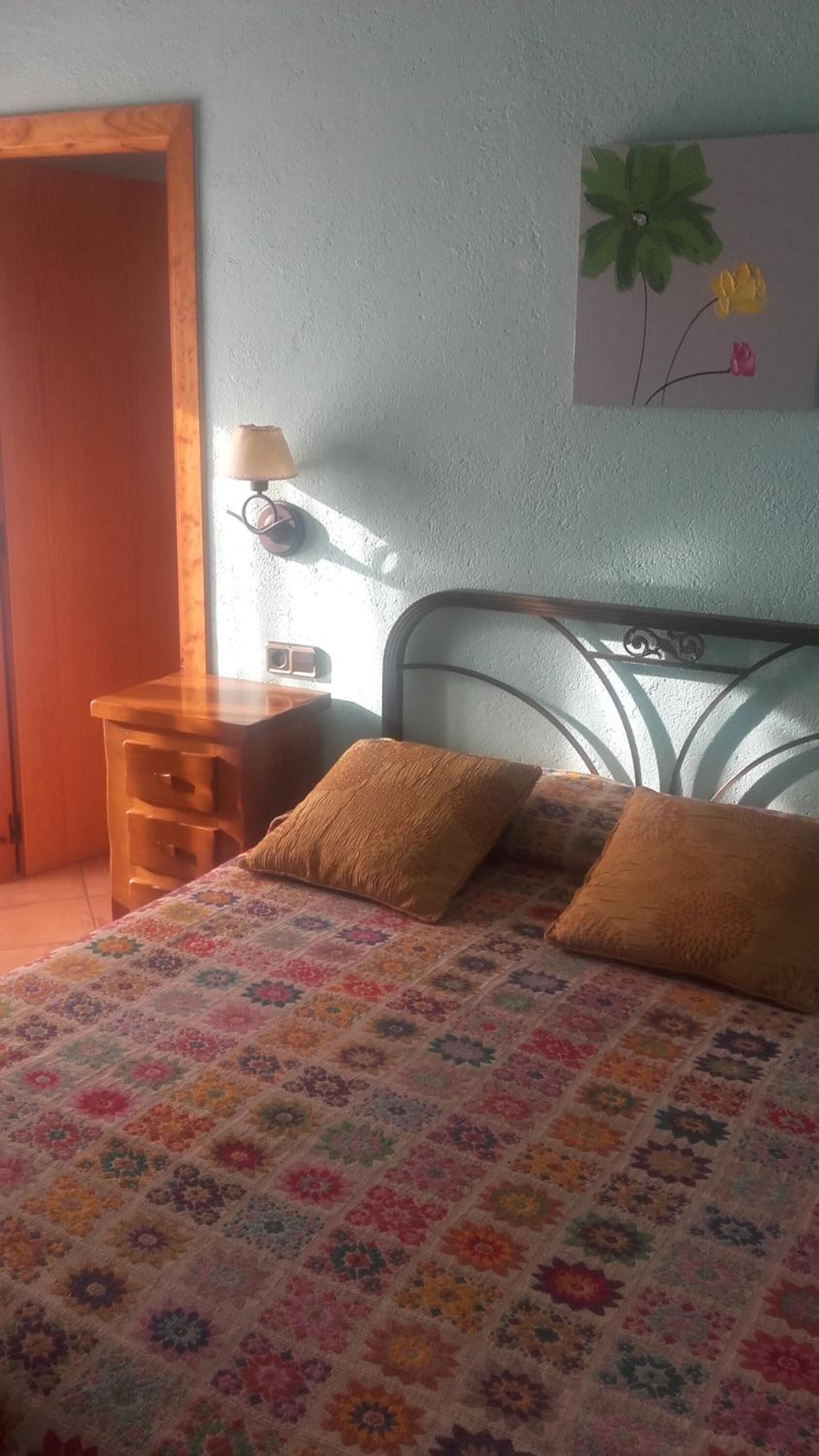 A bedroom with a bed, a nightstand, a lamp, and a wall art piece.