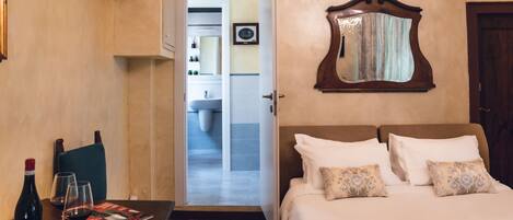 A hotel room with a bed, a table with a wine bottle and glasses, a mirror, and a view into the bathroom.