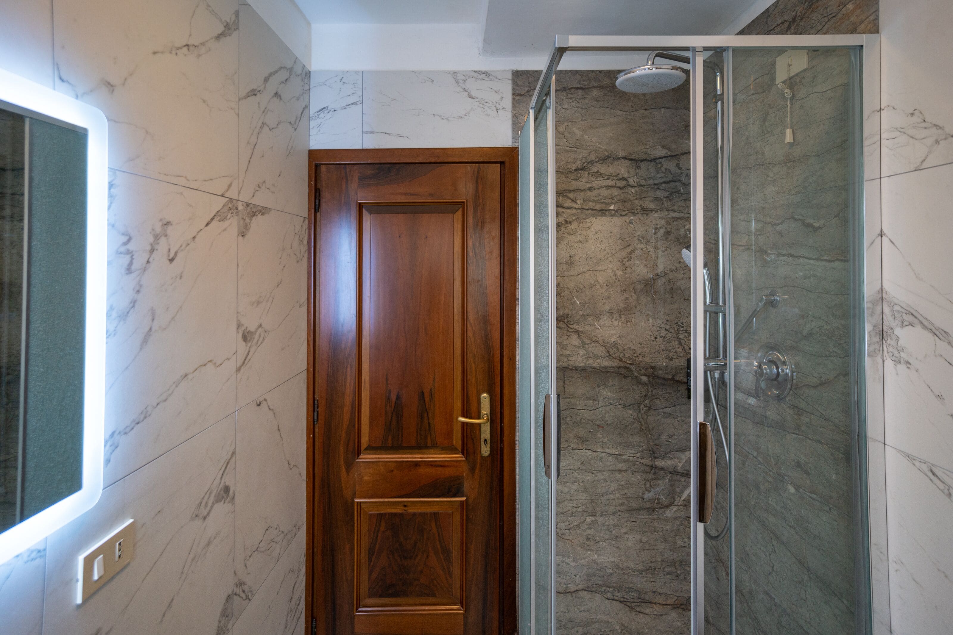 A bathroom with a wooden door, a glass shower enclosure, and marble walls.