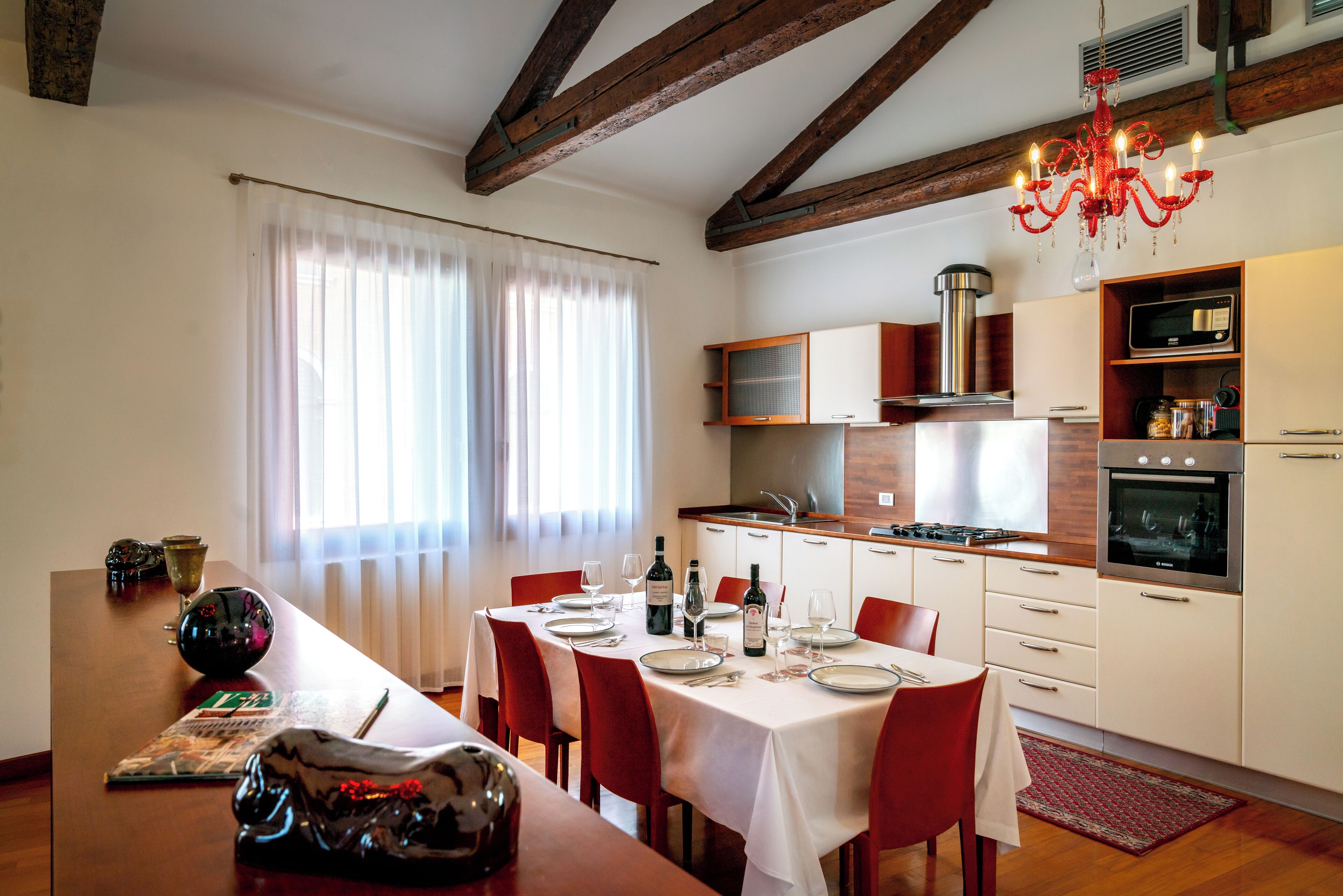 A dining area with a table set for four, red chairs, a chandelier, and a kitchen with modern appliances.