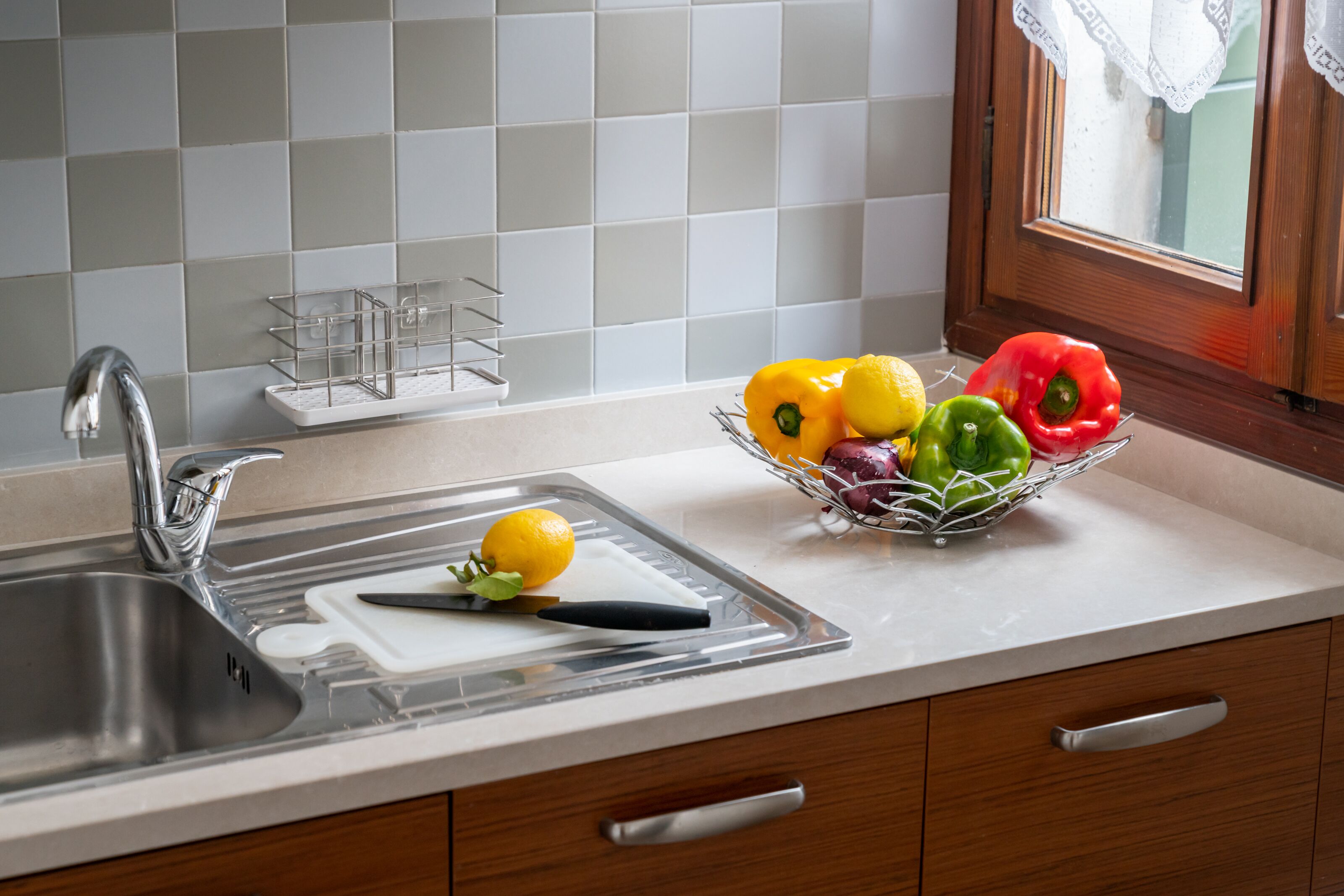 A kitchen with a sink, a cutting board, and a fruit bowl containing lemons, limes, and bell peppers.