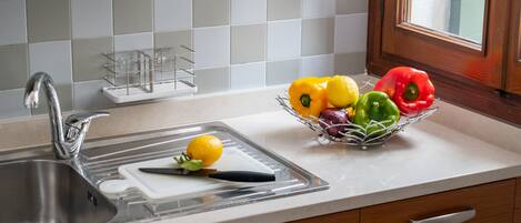A kitchen with a sink, a cutting board, and a fruit bowl containing lemons, limes, and bell peppers.